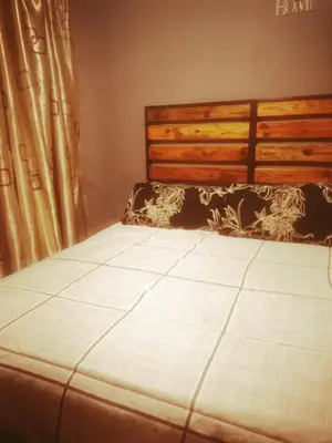 a bedroom with a bed with a wooden headboard and curtains at Baroka Overnight Accommodation in Polokwane