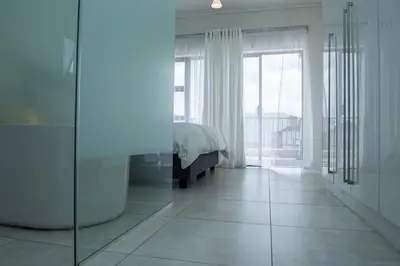a white bedroom with a bed and a large window at Feelathome in Midrand