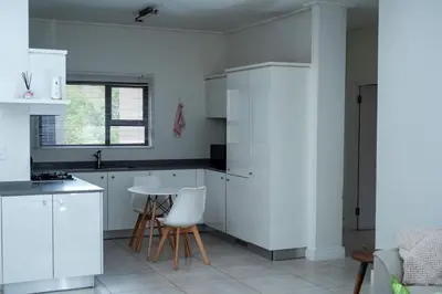 a kitchen with white cabinets and a table and chairs at Feelathome in Midrand