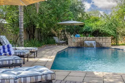 a swimming pool with lounge chairs and an umbrella at Moyres Guest House in Witbank