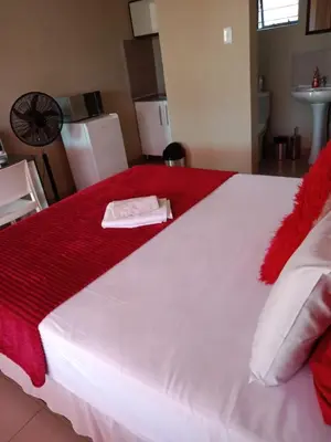 a large white bed with a red blanket on it at Rasesa Guesthouse in Soshanguve