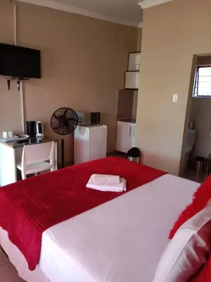 a bedroom with a large white bed with a red blanket at Rasesa Guesthouse in Soshanguve