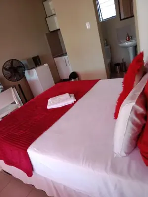 a large white bed with a red blanket on it at Rasesa Guesthouse in Soshanguve
