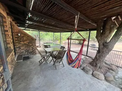a porch with a hammock and a table and a tree at Hello Kruger Hideaway in Marloth Park