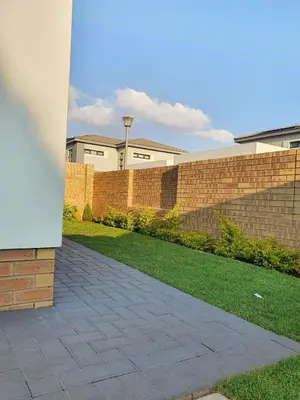 a brick wall and a sidewalk next to a yard at HMT Modern House in Centurion