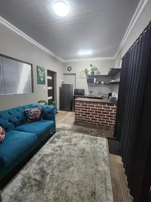 a living room with a blue couch and a kitchen at Ode to Serenity Cottage in Pretoria
