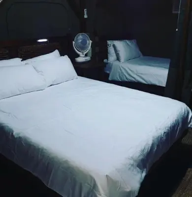 a bedroom with two beds with white sheets and a fan at Sunset Game Farm in Mopane