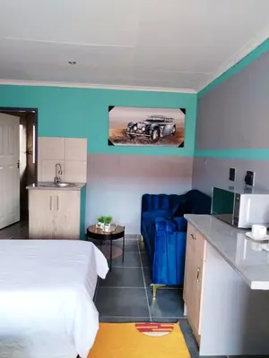 a room with a bed and a kitchen with a car on the wall at Reutlwane Gardens B&B in Secunda