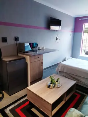 a room with a bed and a kitchen and a table at Reutlwane Gardens B&B in Secunda