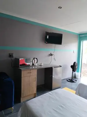 a room with a bed and a desk and a tv on the wall at Reutlwane Gardens B&B in Secunda