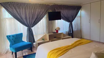 a bedroom with a bed and a blue chair and window at ekhaya guesthouse in Secunda