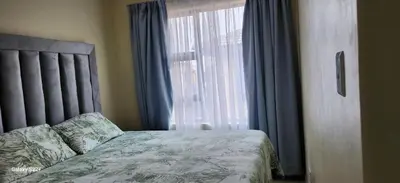 a bedroom with a bed and a window with blue curtains at Cloveridge 104 in Benoni