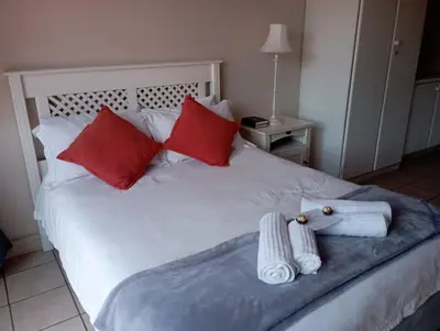 a white bed with red pillows and towels on it at Bloemhoek Guest House in Centurion