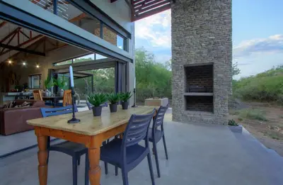 a patio with a wooden table and chairs and a fireplace at IHLATHi Glass Dome in Marloth Park