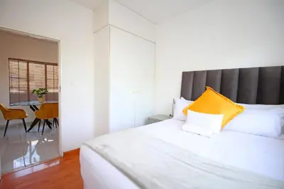 a bedroom with a large white bed with an orange pillow at VH Apartments have fun with us in Midrand