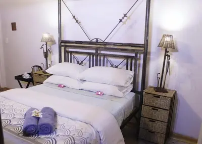 a bedroom with a bed with white sheets and purple towels at Canimambo at The Old Post Office Inn in Graskop