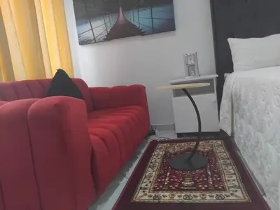 a living room with a red couch next to a bed at Claremont Secured Accommodation in Pretoria