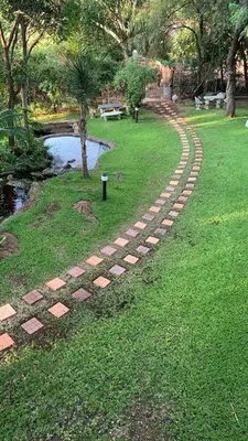 a brick path in a park next to a pond at The Palace Guest House in Pretoria