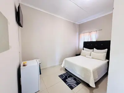 a small bedroom with a white bed and a tv at Relax Guest House in Ermelo