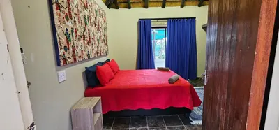a bedroom with a red bed with blue curtains at The Rondawel in Marloth Park