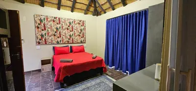 a bedroom with a red bed and blue curtains at The Rondawel in Marloth Park