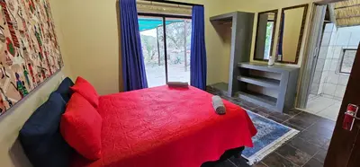 a bedroom with a red bed and a window at The Rondawel in Marloth Park