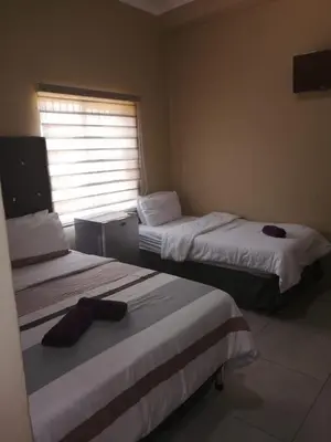 two beds in a hotel room with a window at Royal guest lodge in Middelburg