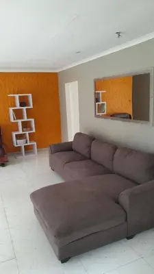 a living room with a brown couch and a mirror at Emasimini Cottages in Midrand