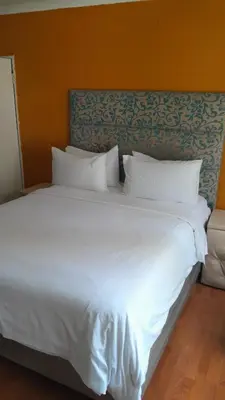 a large bed with white sheets and pillows at Emasimini Cottages in Midrand