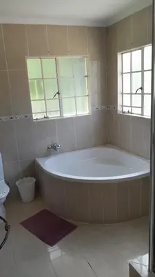 a large white tub in a bathroom with two windows at Emasimini Cottages in Midrand