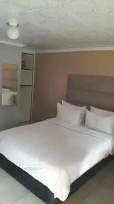 a large bed with white sheets and pillows at Emasimini Cottages in Midrand