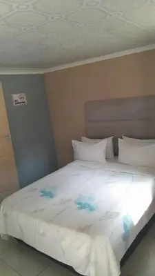 a bed with white sheets and blue flowers on it at Emasimini Cottages in Midrand