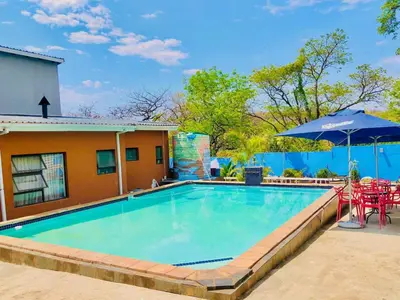 a swimming pool with tables and chairs and an umbrella at Woodpecker's Guest House in Hazyview