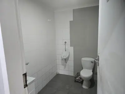 a white bathroom with a toilet and a urinal at The Chardonay Inn in Centurion