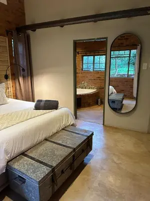a bedroom with a bed and a mirror and a tub at Wild Fig Cottage with Tickle Tub in Hartbeespoort in Pelindaba