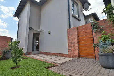 a white house with a brick wall and a fence at Perfect Hideaway in Nelspruit