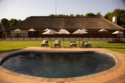 a swimming pool with chairs and umbrellas in front of a building at Ingaadi in Pretoria