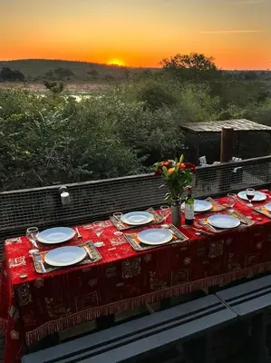 a table with plates and flowers on it with the sunset at Ingwenya View in Marloth Park
