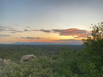 a sunset over a field with a rock and trees at Harmonie Hills in Sukani