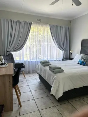 a bedroom with a bed and a desk and a window at Afrisky Guest House in Kempton Park