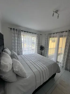 a bedroom with a bed with white sheets and windows at Home away from Home in Midrand
