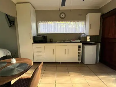 a kitchen with a table and a sink and a refrigerator at Lazy Trail Cottage in Nelspruit