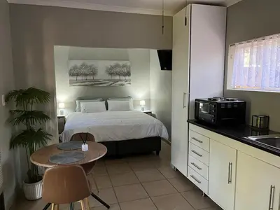 a bedroom with a bed and a table and a kitchen at Lazy Trail Cottage in Nelspruit