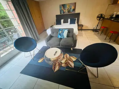 a bedroom with a bed and two chairs and a couch at Mbizo Cozy Retreat- Lofts at Loftus in Pretoria