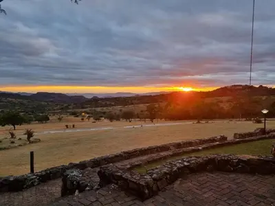 a sunset in a field with the sun setting in the distance at Klipspringer Lodge in Nelspruit