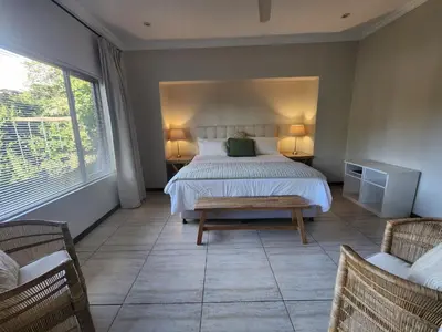 a bedroom with a bed and two chairs and a window at Maclarty House - Golf Estate Villa in White River