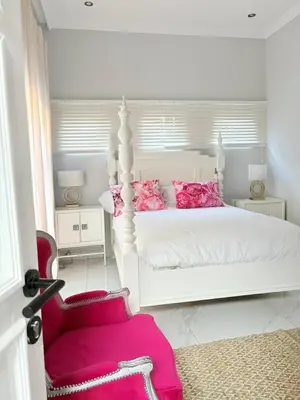 a white bedroom with a white bed with pink pillows at View at 81 in Hartbeespoort