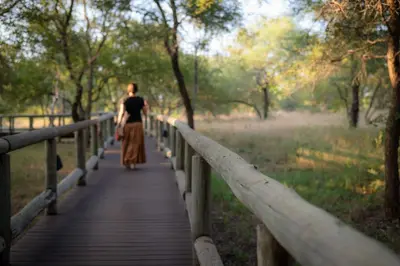 a woman walking down a wooden bridge at Xidulu Safari Lodge - Makalali in Makalali Game Reserve