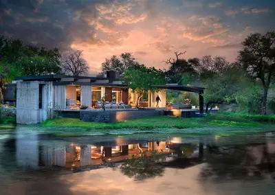 a house on the edge of a river at sunset at Cheetah Plains Private Game Reserve in Sabi Sand Game Reserve