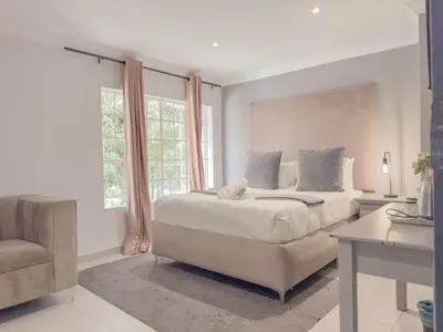 a white bedroom with a large bed and a chair at Amoris Guesthouse - Hillcrest Brooklyn in Pretoria